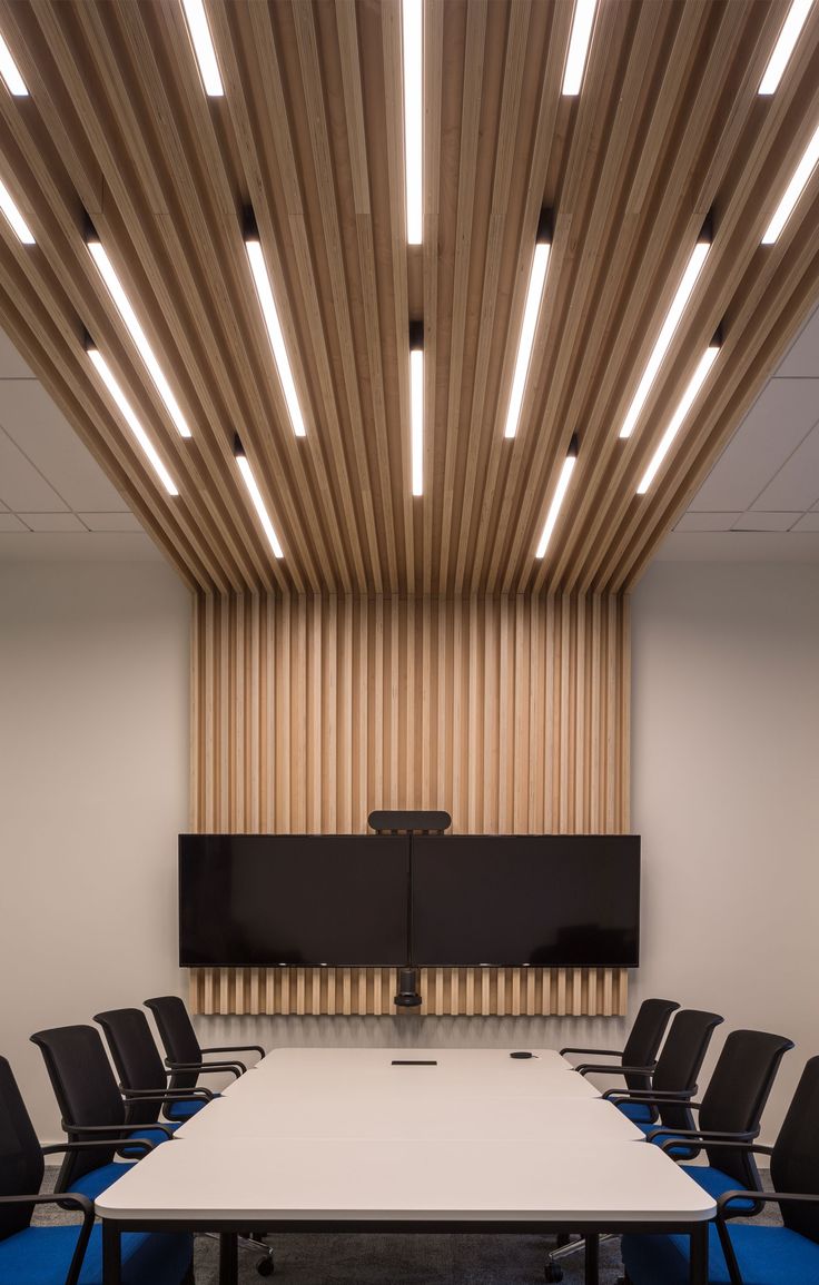 an empty conference room with blue chairs and a white table in front of a wooden paneled wall