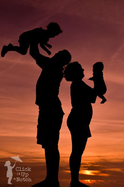 the silhouette of a man and woman holding a child at sunset