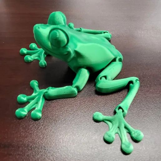 a green toy frog sitting on top of a wooden table next to a black object