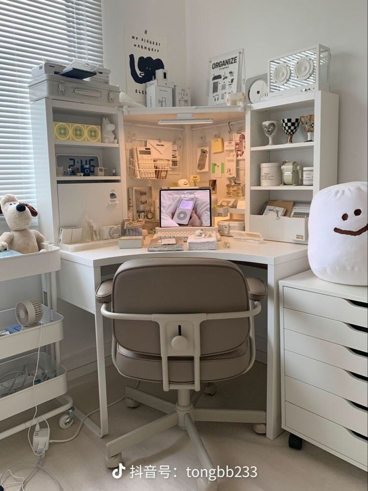 a white desk topped with a computer monitor next to a stuffed animal on top of a chair