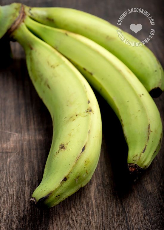 three green bananas sitting on top of a wooden table