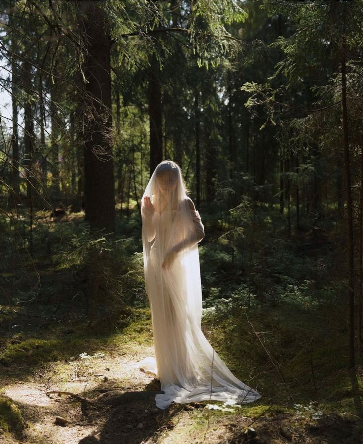 a woman in a white dress is standing in the woods with her back to the camera