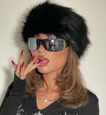 a woman wearing sunglasses and a fur hat with her finger in the air while making a funny face