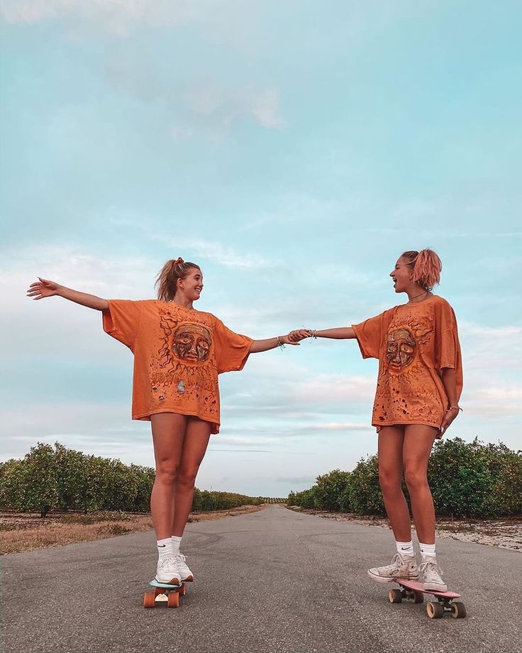 two girls in orange dresses are skateboarding down the road together with their arms outstretched