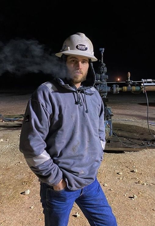 a man wearing a hat standing in front of a train at night with steam coming from it