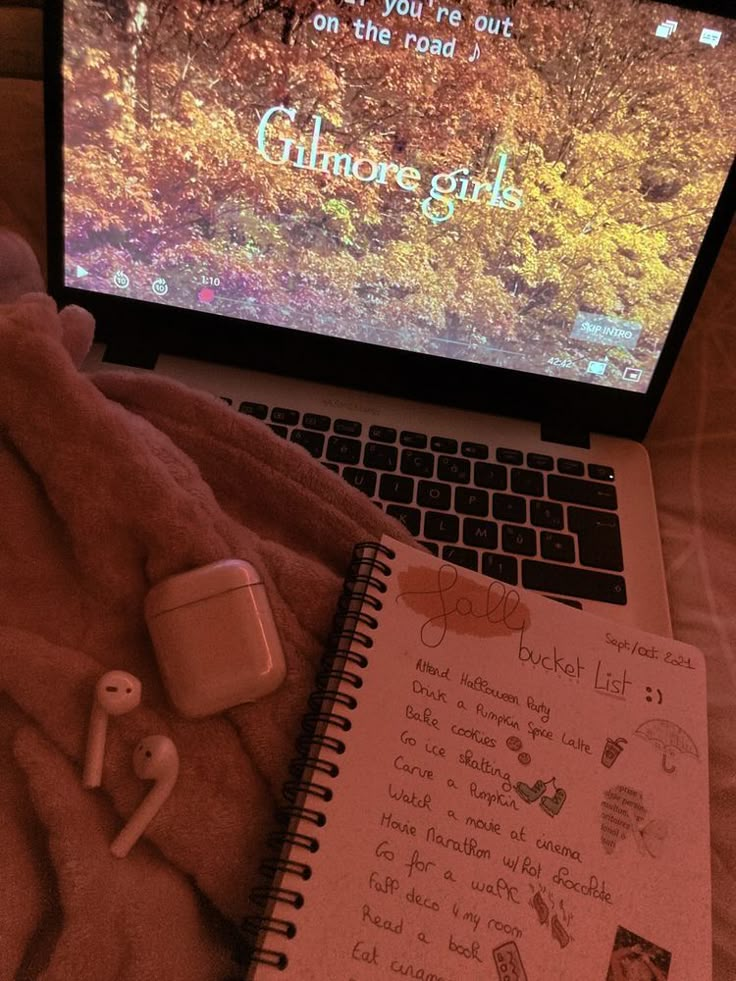 an open laptop computer sitting on top of a bed next to a notepad and earbuds