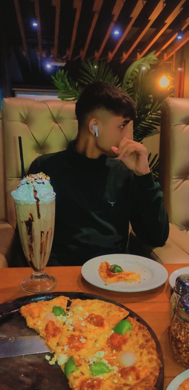 a man sitting in front of a pizza on top of a table next to a drink