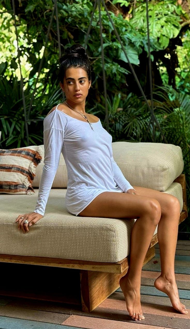 a woman sitting on top of a wooden bench in front of some plants and trees