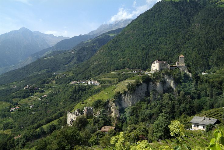 a small village on the side of a mountain with green trees and mountains in the background