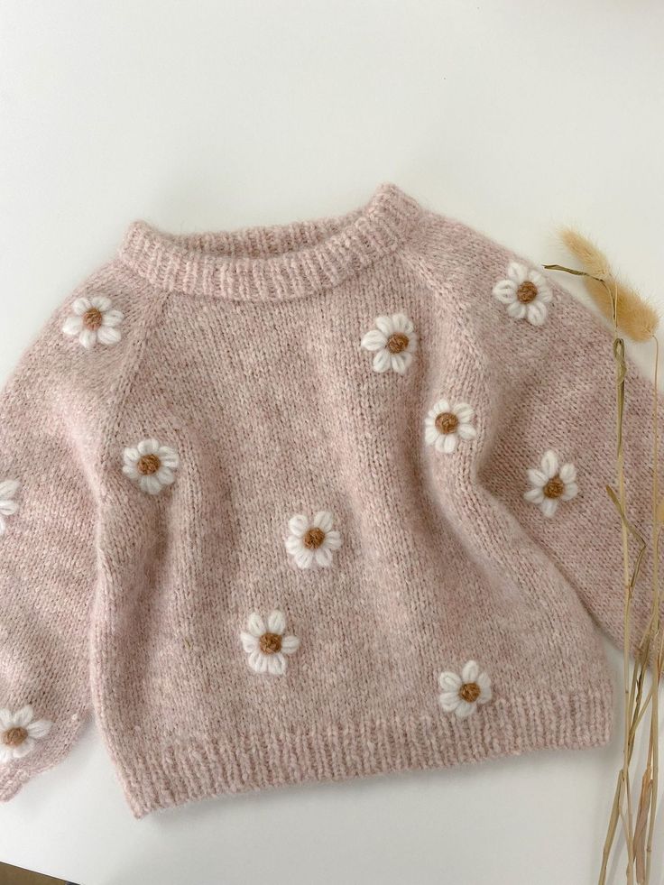 a pink sweater with white flowers on it and some dried grass in the foreground