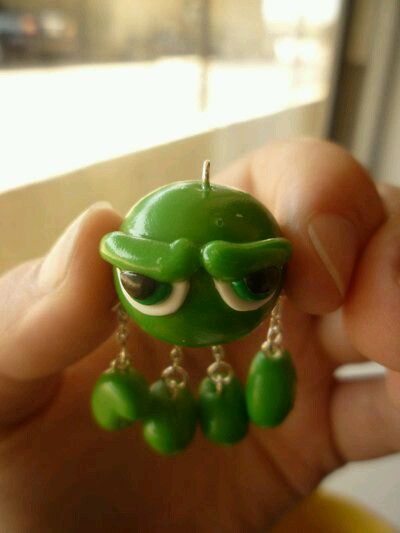 a person holding a small green toy with eyes and earring clips in their hand