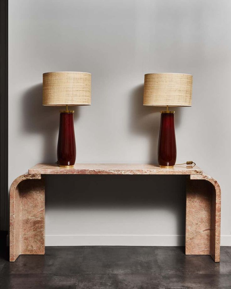 two lamps sitting on top of a wooden table next to each other in front of a white wall