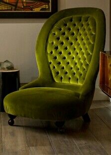 a green velvet chair sitting on top of a hard wood floor next to a painting