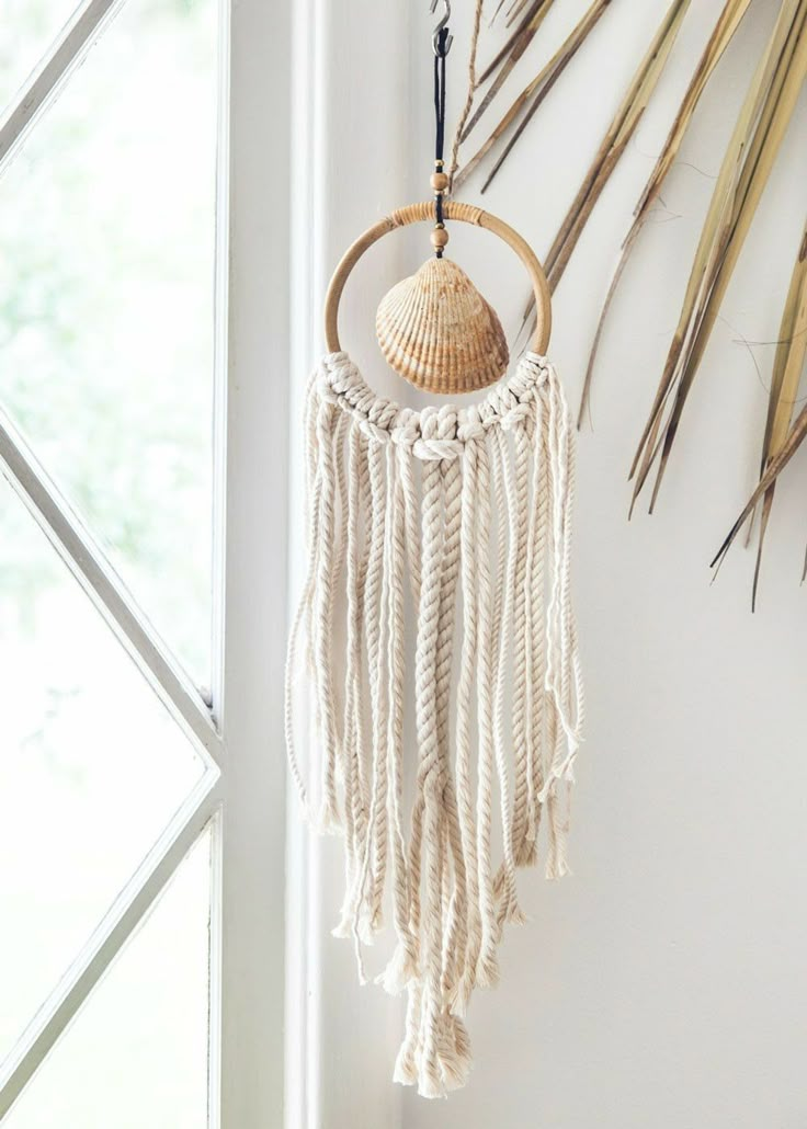 a white wall hanging next to a window filled with dried grass and palm leaves on it