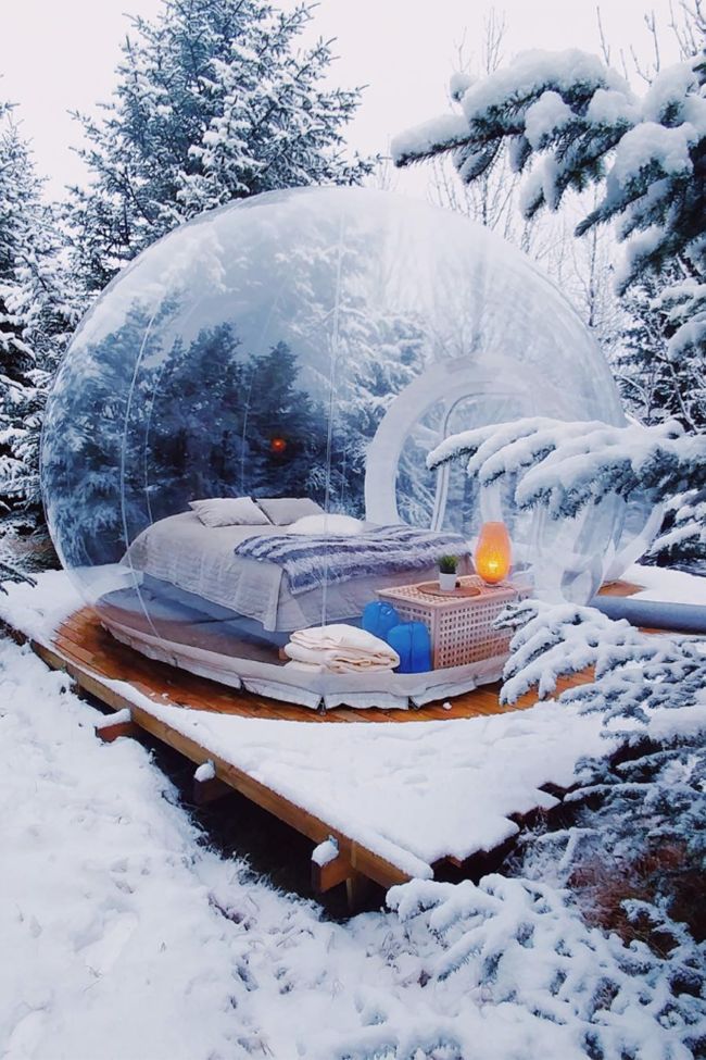 an inflatable bubble bed sits on a wooden platform surrounded by snow covered trees