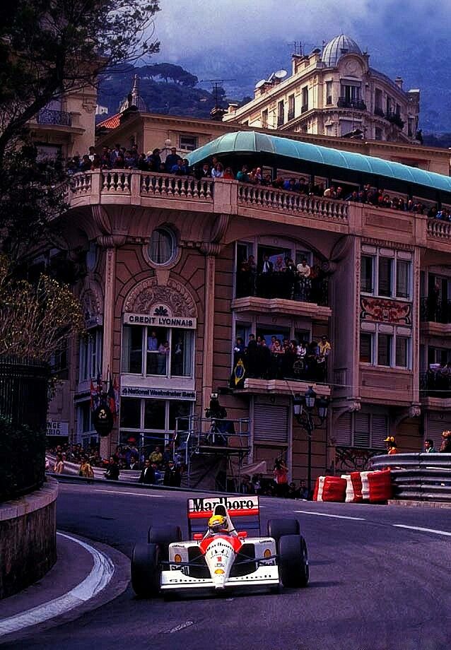 a man driving a race car down a street in front of a tall, ornate building