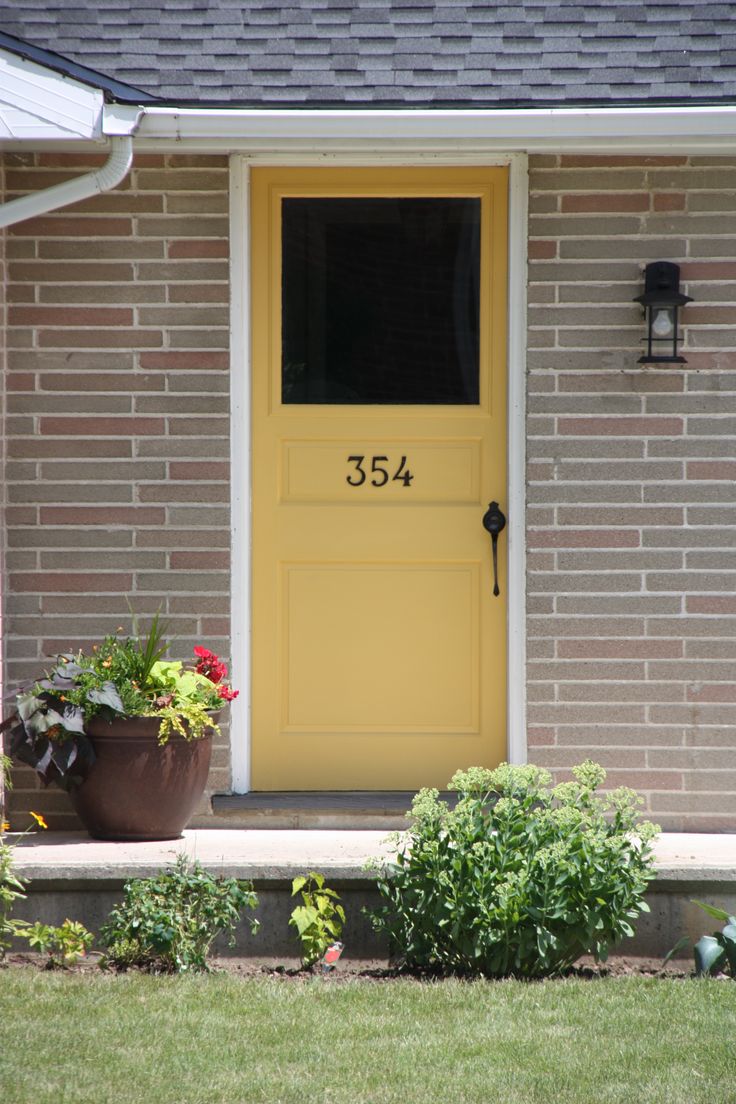 a yellow front door on a brick house with two planters in the foreground