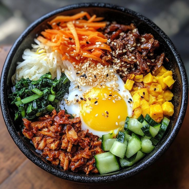 a bowl filled with meat, vegetables and an egg on top of some sort of rice