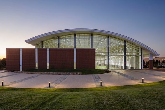 an empty building lit up at night with lights on the ground and grass in front