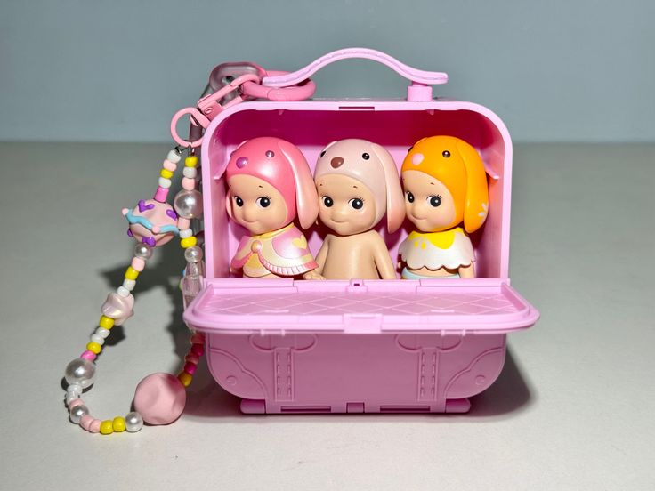 a pink toy case with three little dolls in it