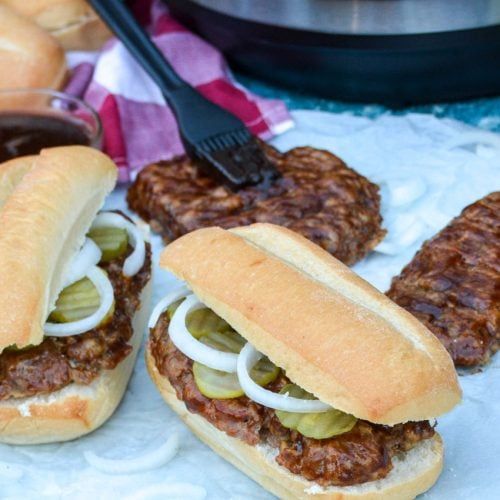 two hot dogs with onions and pickles in buns next to some other food