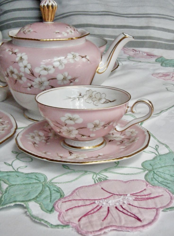 a pink tea set with matching saucers and cups on a floral tablecloth,