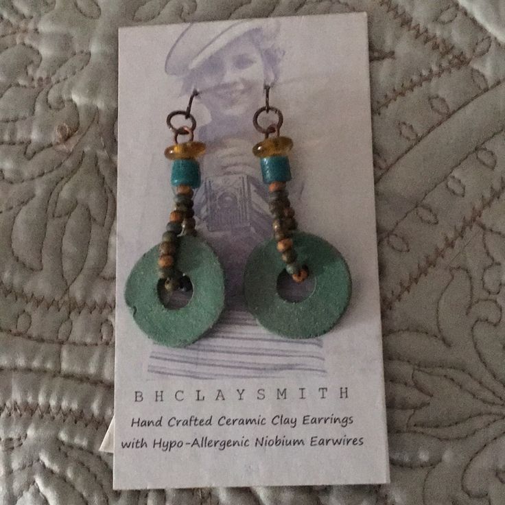 a pair of earrings with beads on them sitting on top of a bed next to a piece of paper