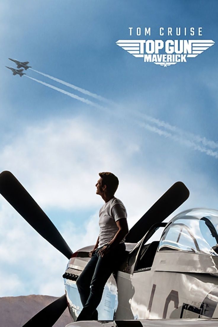 a man sitting on the wing of an airplane looking up at a plane in the sky