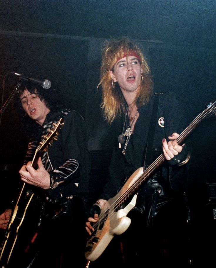 two young men playing guitars in front of microphones