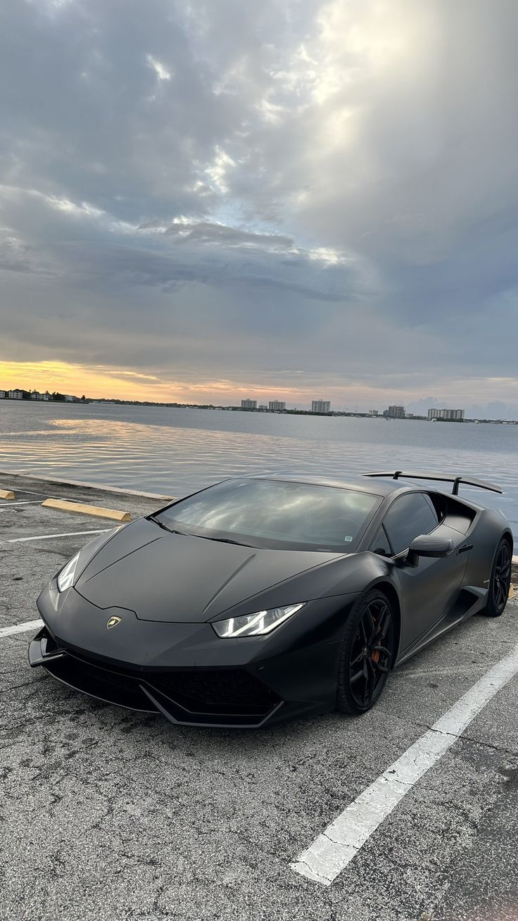 a black sports car parked in a parking lot next to the ocean at sunset or dawn