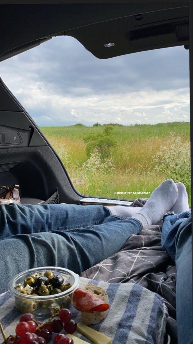 a man laying in the back of a truck next to a bowl of fruit and cheese