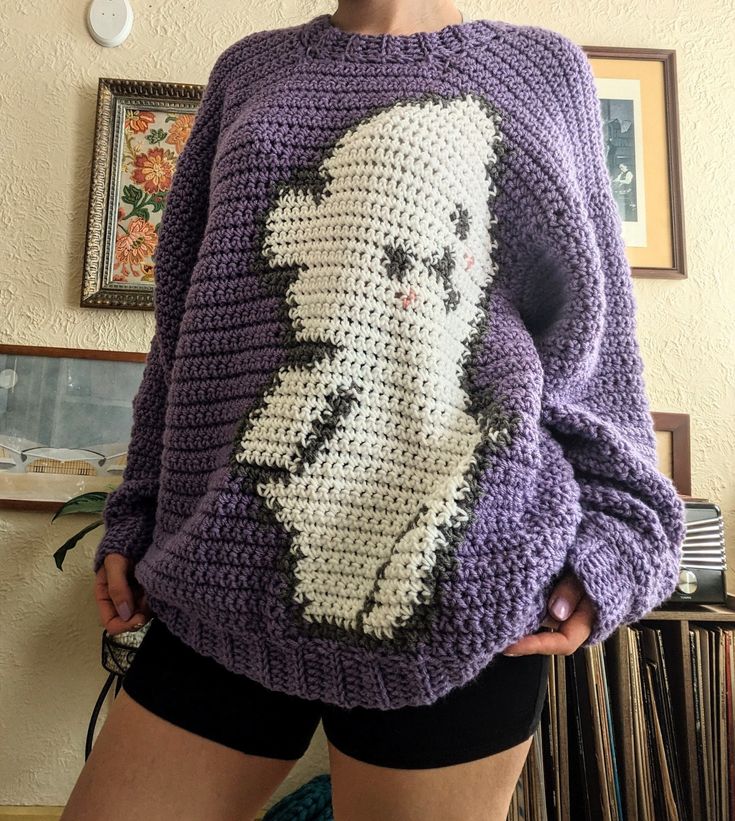 a woman is wearing a crocheted sweater with an image of a cat on it