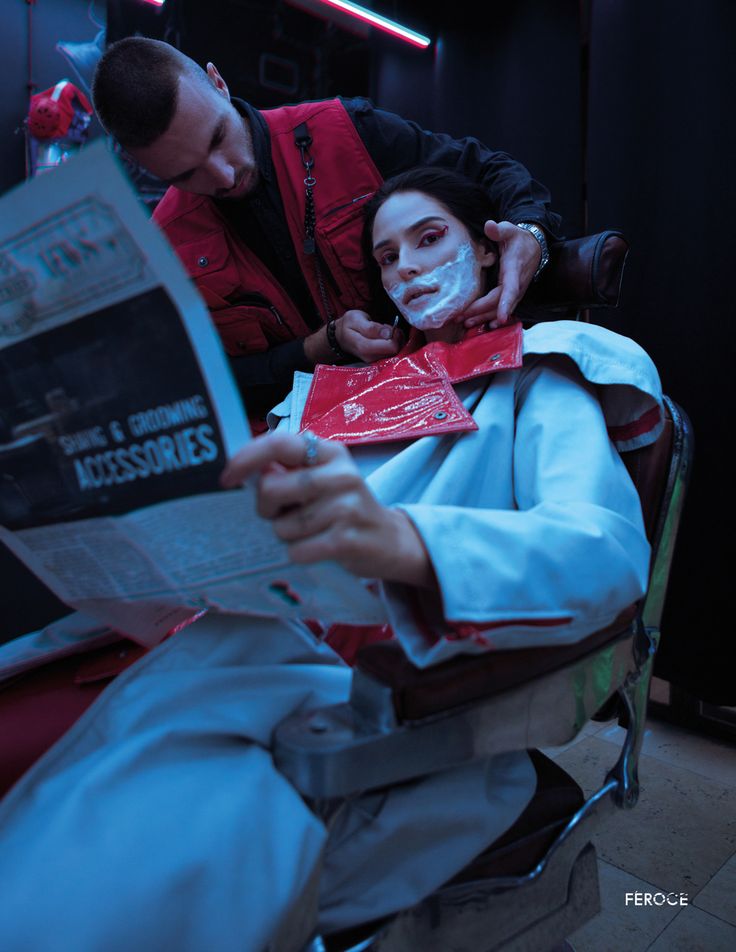 a man is shaving his face while sitting in a chair next to a woman