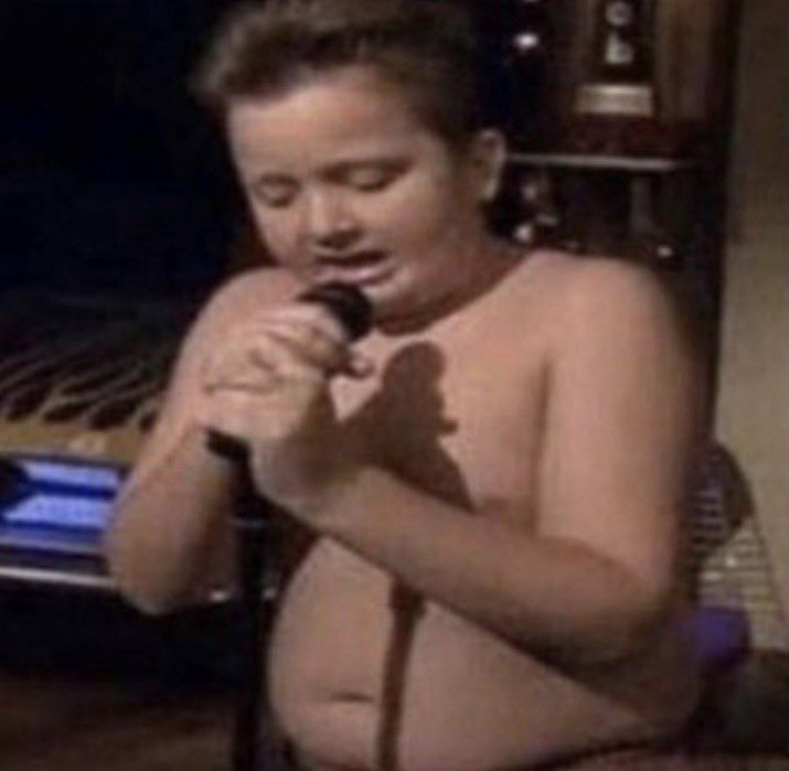 a shirtless boy holding a microphone in front of an open oven with the door open