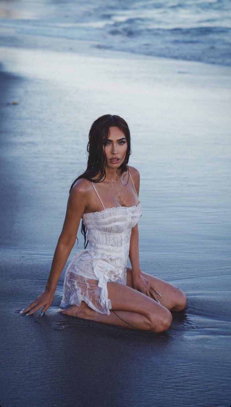 a woman sitting on the beach in a white dress