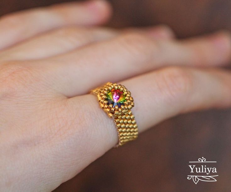 a woman's hand wearing a gold ring with a multicolored diamond on it