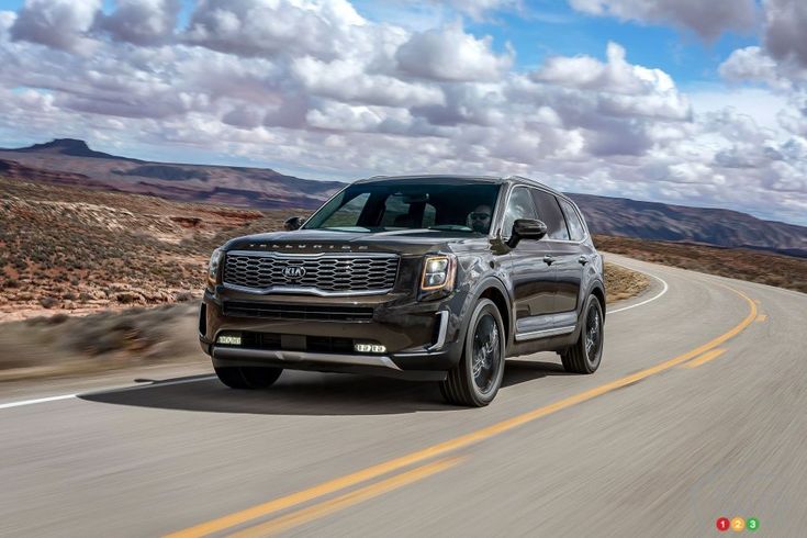 the front end of a black suv driving down a road with mountains in the background