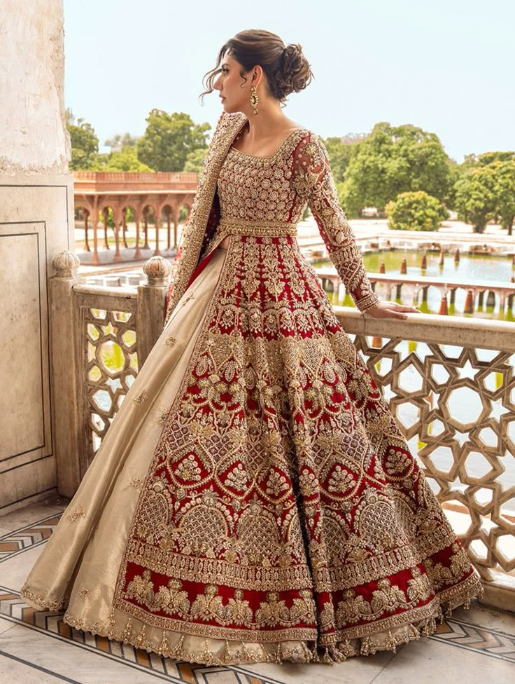 a woman in a red and gold wedding gown standing on a balcony looking at the water