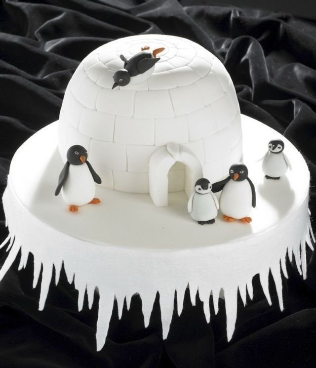 an igloose cake decorated with penguins and icing on a black tablecloth