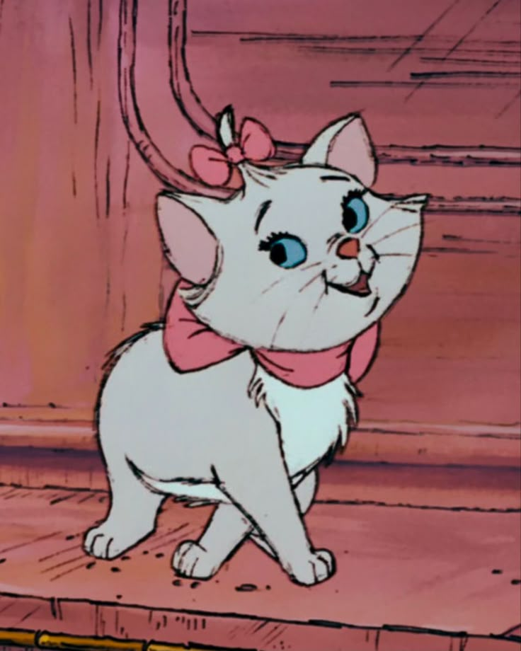 a white cat with a pink bow on its head standing in front of a door