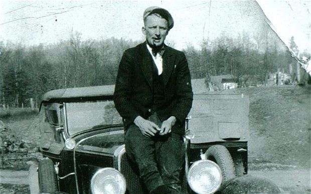 an old black and white photo of a man sitting on the hood of a car