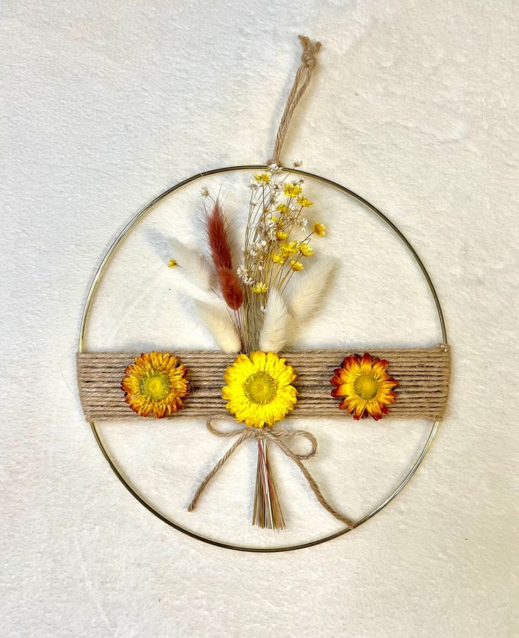 a circular metal wall hanging with flowers on it's side and dried grass in the center