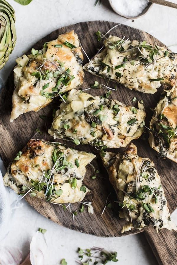 several pieces of pizza sitting on top of a wooden cutting board next to an artichoke