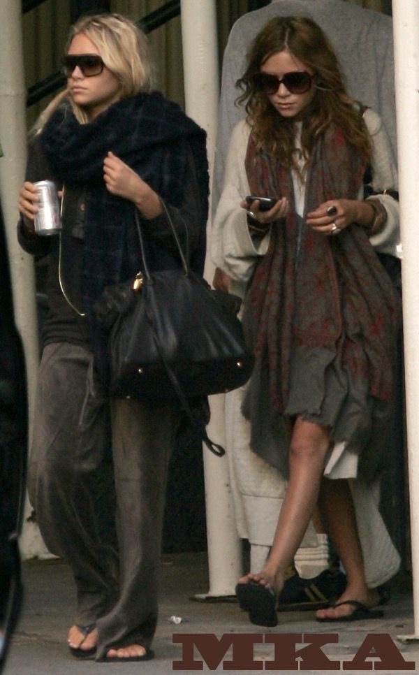 two women walking down the street with one holding a coffee cup and another looking at her cell phone