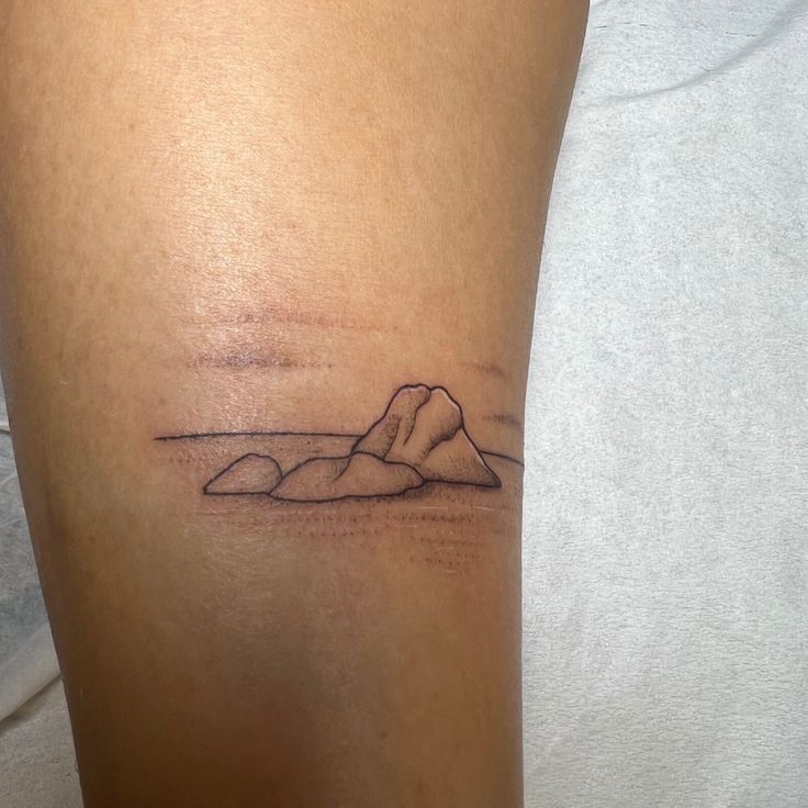 a woman's leg with a small tattoo of a mountain in the distance on it