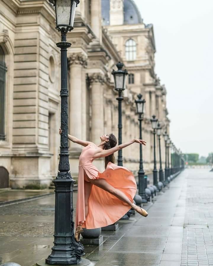 a ballerina leaning against a lamp post on the sidewalk in front of an old building