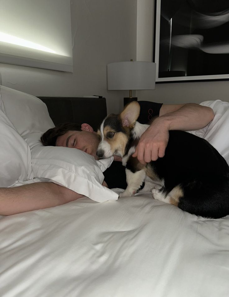 a man laying in bed with a dog on his chest and one arm around him