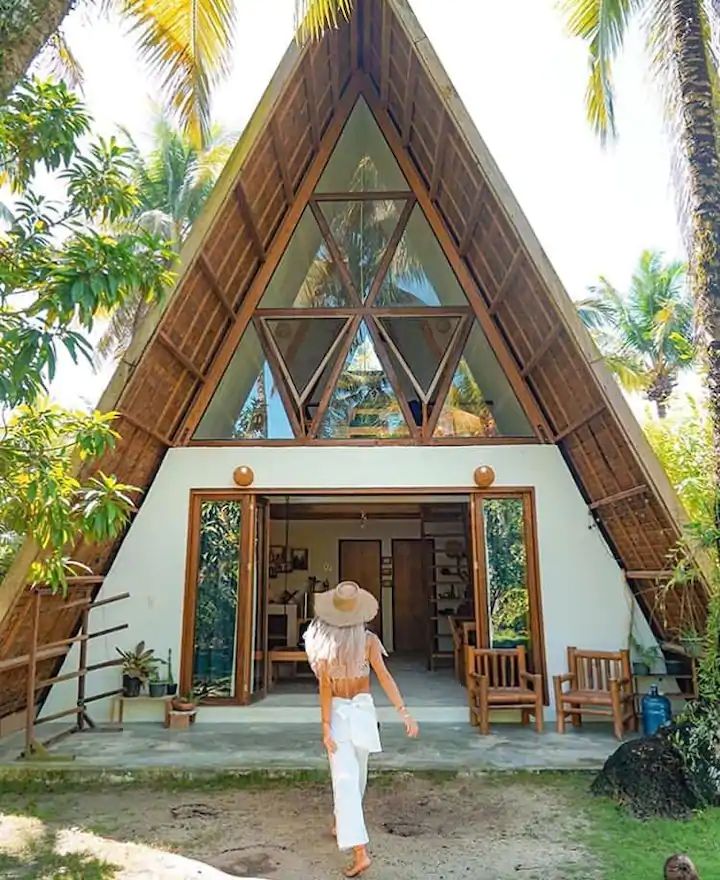 a woman walking towards a house with a large triangular roof