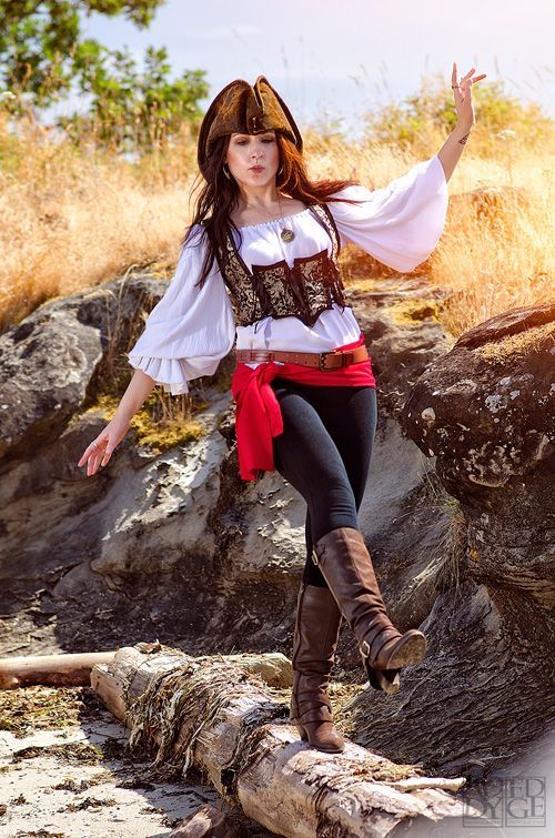 a woman dressed in pirate clothing posing on a log with her arms outstretched and hands out