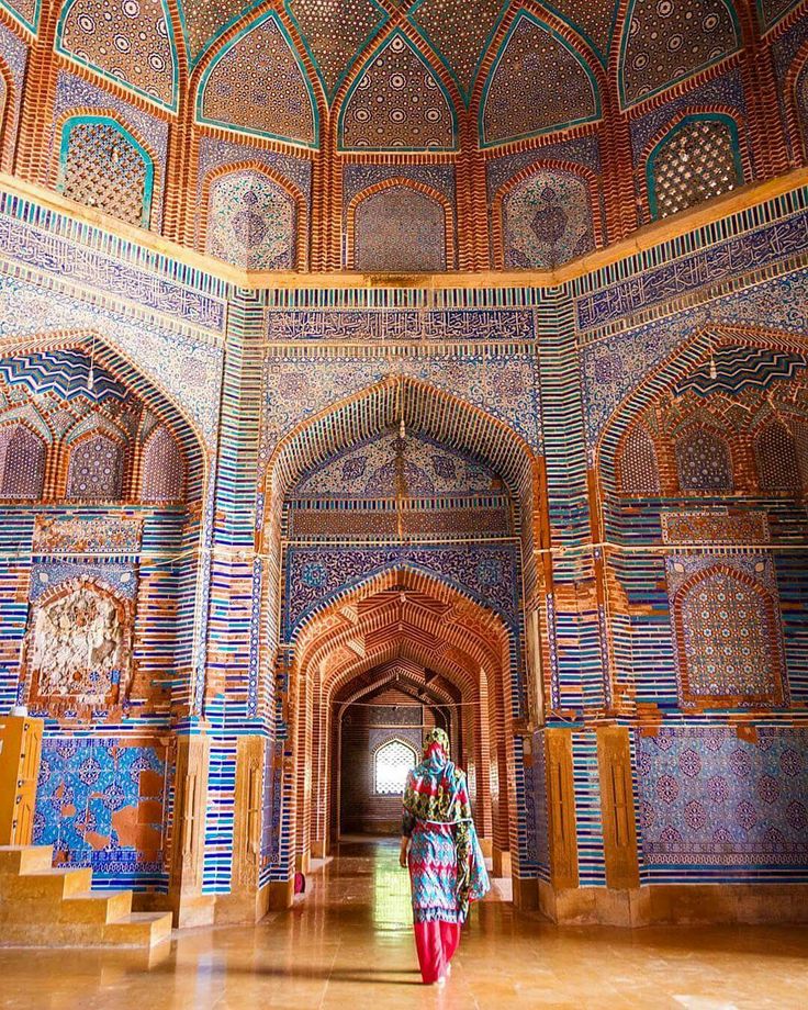 a woman is walking through an ornately decorated building with blue and red tiles on the walls